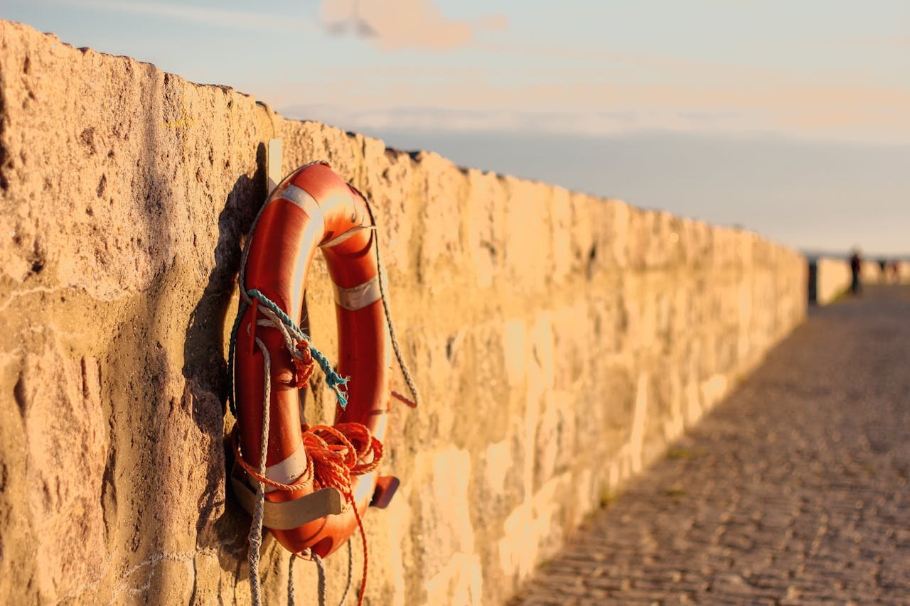 Vibrant lifebuoy hung on a stone seawall under golden sunset light by the beach.